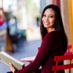 Woman sitting down holding a book a looking over her left shoulder to smile.