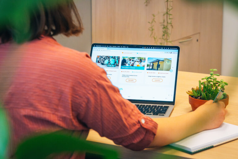 Woman sitting at a desk on a laptop looking at the BeWell Events page.