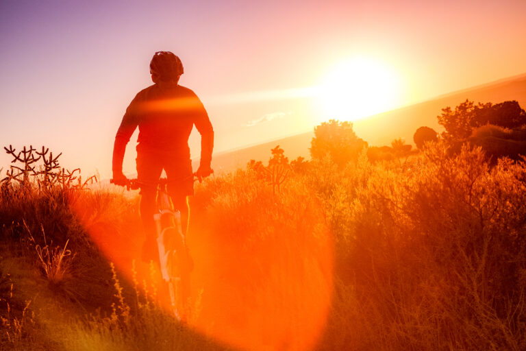 man riding mountain bike silhouetted against sunshine lens flare while riding in the desert landscape of the sandia mountains. horizontal composition.